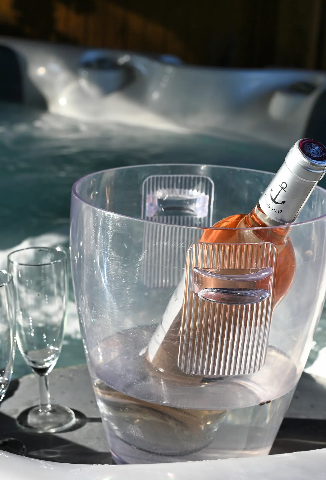Deux flûtes et une bouteille de rosé dans son seau, posées au bord du jacuzzi qui bouillonne