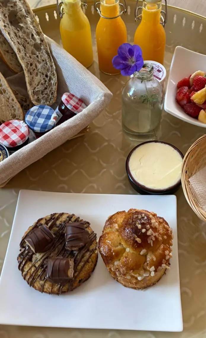 Le plateau du matin : pain au levain, confitures et beurre, jus d’orange pressé, salade de fruits frais, pain au chocolat, un cookie au chocolat et une brioche