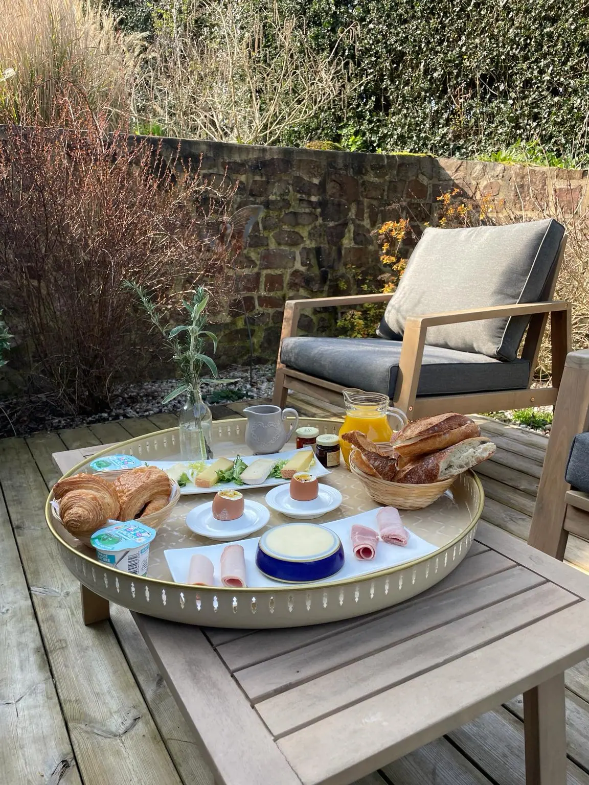 Le plateau du brunch servi dehors, sur la table basse d’une terrasse du Hameau : croissants, fromages, jambon, œufs à la coque, pain, confitures et jus d’orange pressé