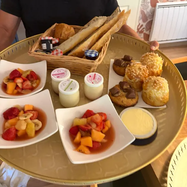 Un plateau doré avec des salades de fruits frais, des yaourts, des chouquettes, des viennoiseries, un panier de pain et des petits pots de confiture