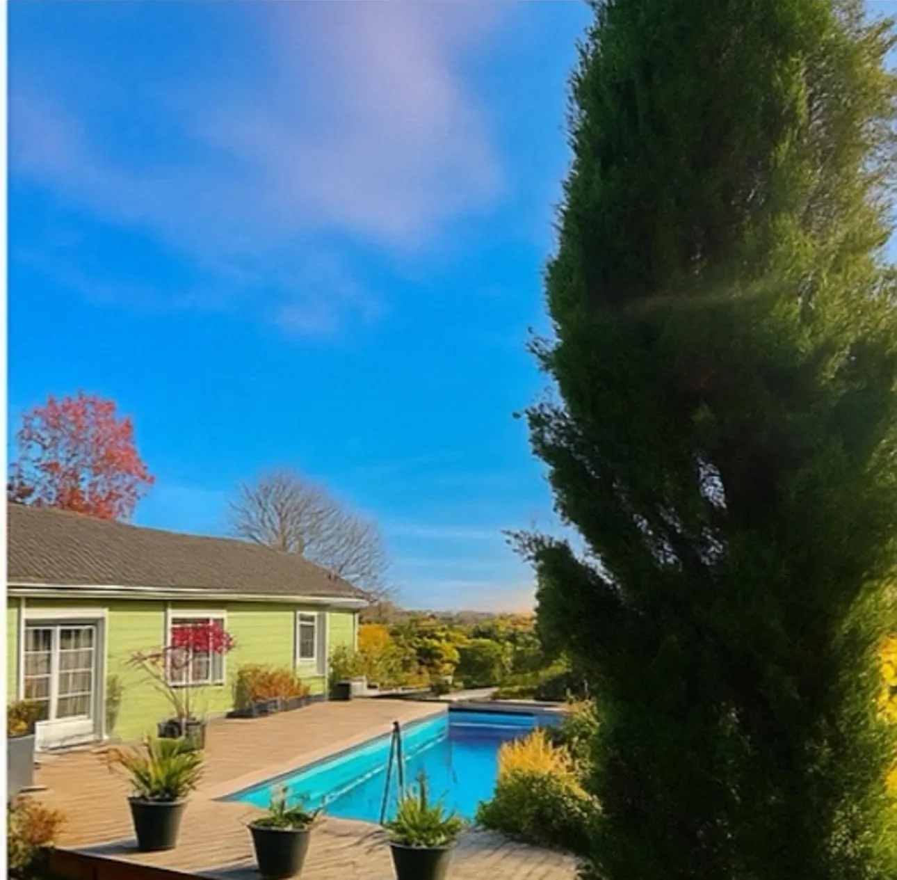 La piscine au pied du Chalet Normand, le grand cyprès et un ciel d’automne