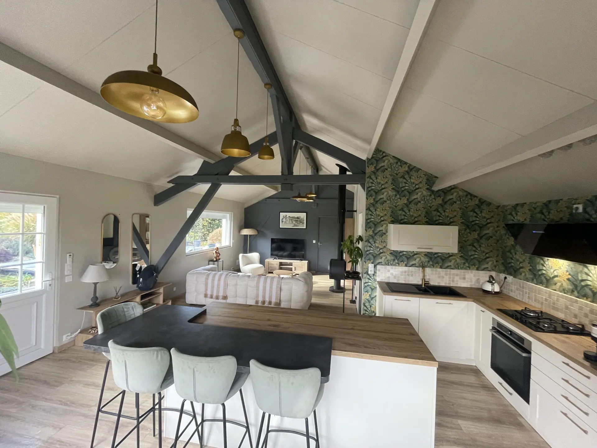 La pièce à vivre du Chalet Normand, son îlot et ses tabourets, sous la charpente grise