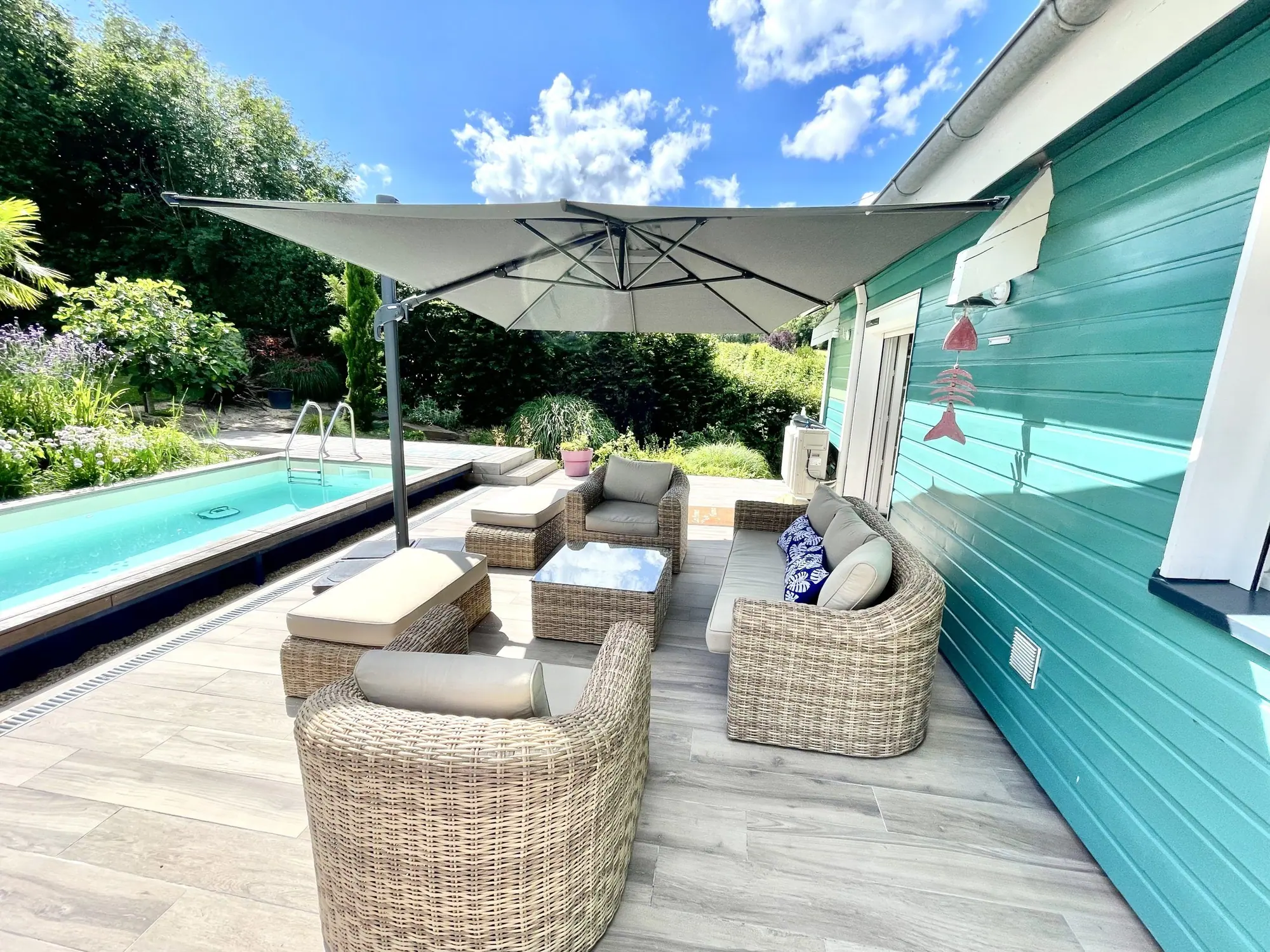 La terrasse du Chalet Normand, le salon de jardin sous le parasol, la piscine le long du chalet