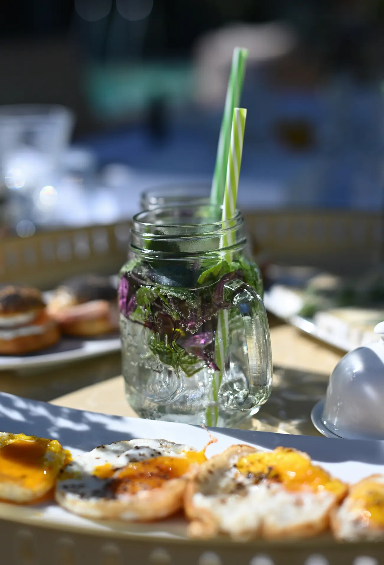 Un bocal d’eau aux herbes et ses deux pailles, sur la table du petit-déjeuner servi dehors