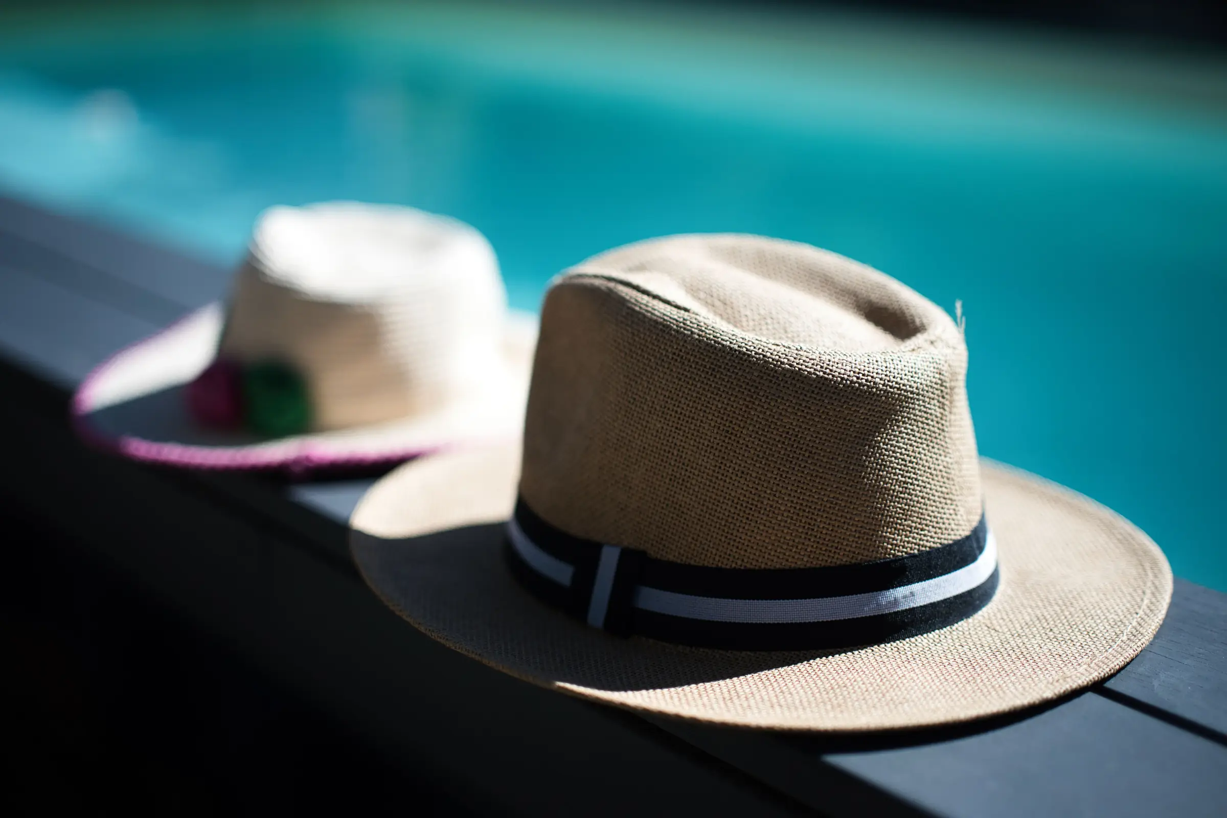 Two straw hats resting on the edge of the Chalet Normand’s heated pool, the turquoise water behind