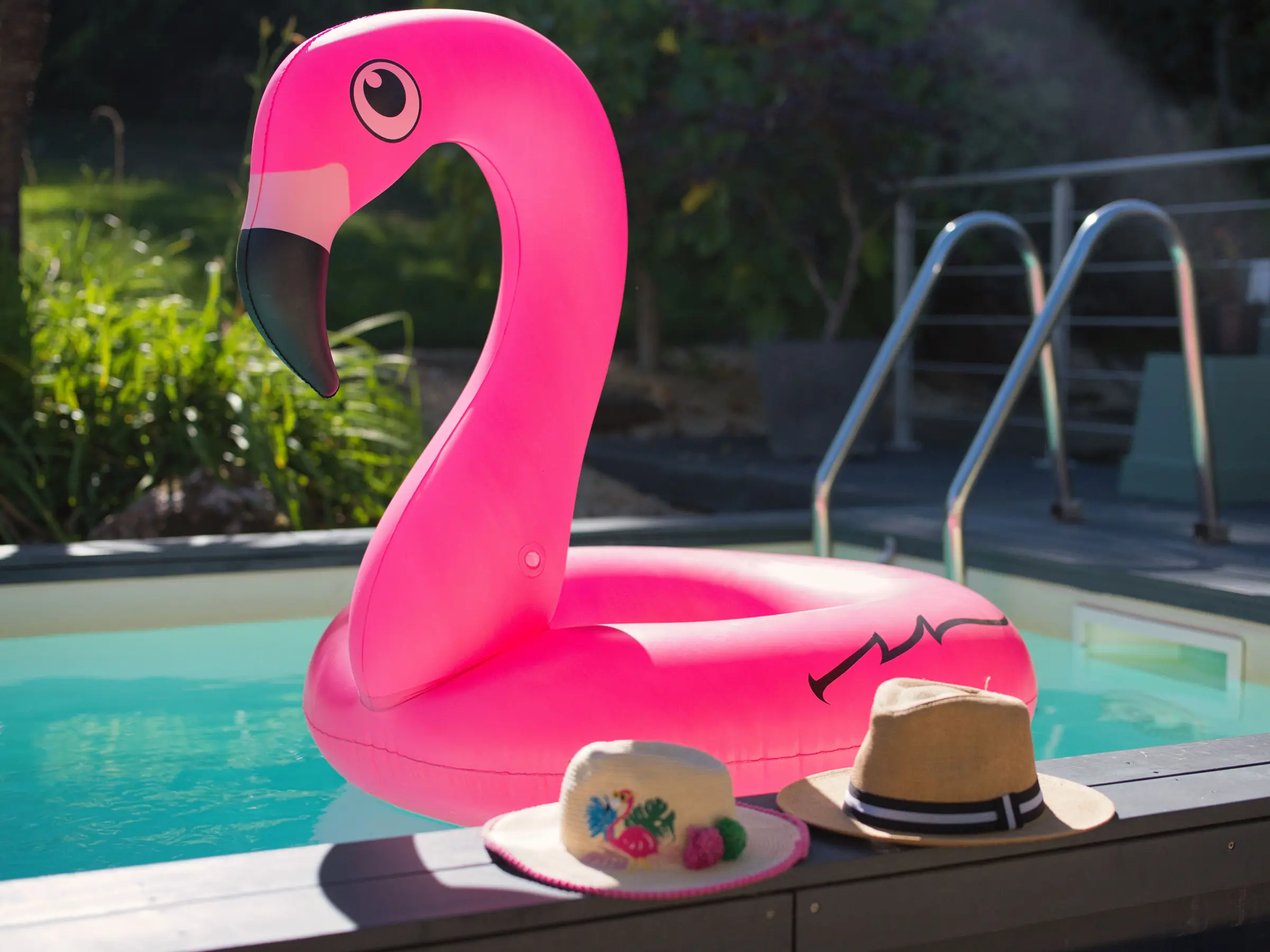 La bouée flamant rose et un chapeau de paille au bord de la piscine chauffée, l’échelle du bassin derrière