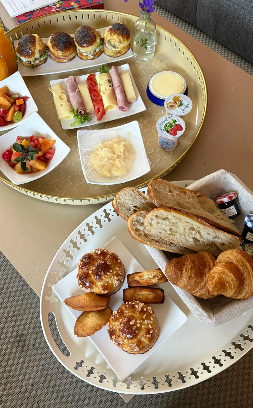 Le mixte sur la table du salon : un plateau de buns, charcuterie et fruits, un autre de pain, croissants, brioches et madeleines