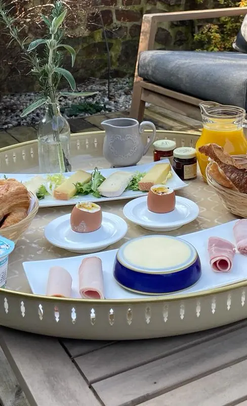 Le brunch servi dehors, sur la table basse d’une terrasse : croissants, fromages, œufs à la coque, pain et jus d’orange