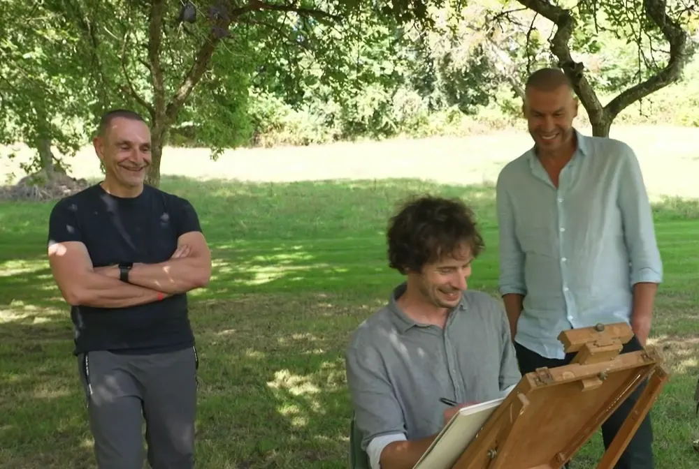 Cyp rit à son chevalet sous un arbre du jardin, deux hommes le regardent dessiner