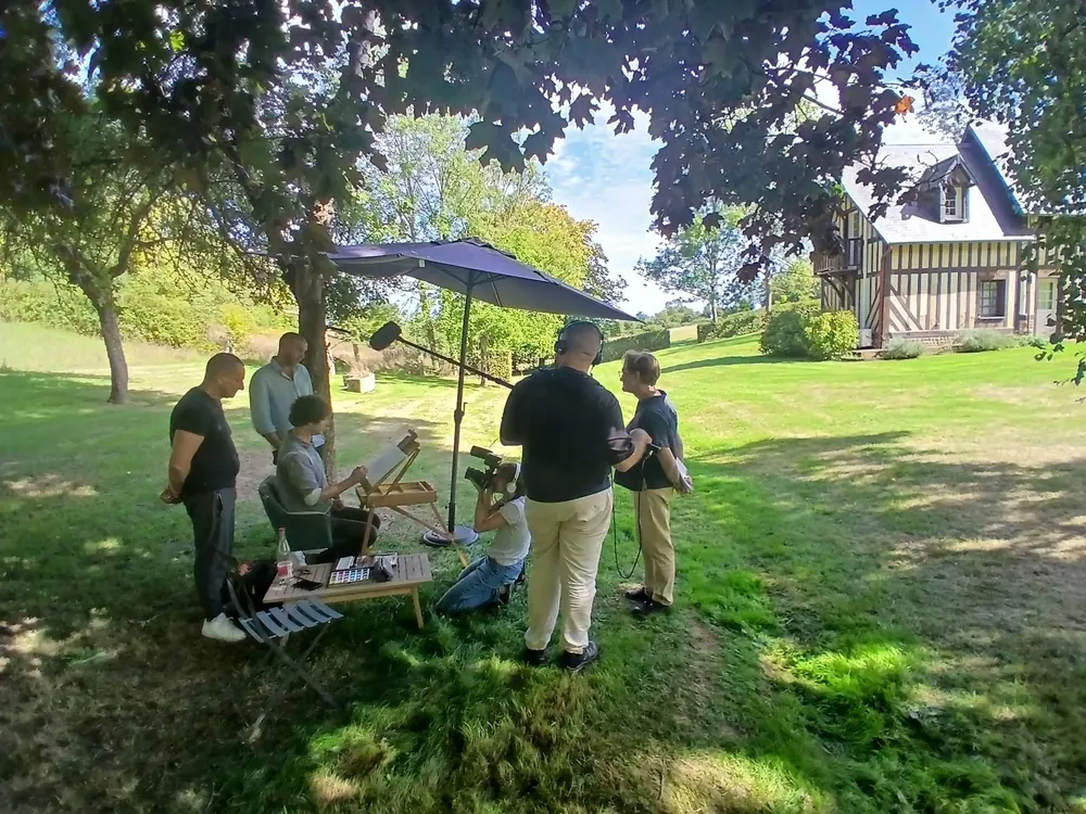 L’équipe de France 2 sous un parasol du jardin, caméra et perche tendues vers Cyp à son chevalet, Reinette Grise au fond de la pelouse