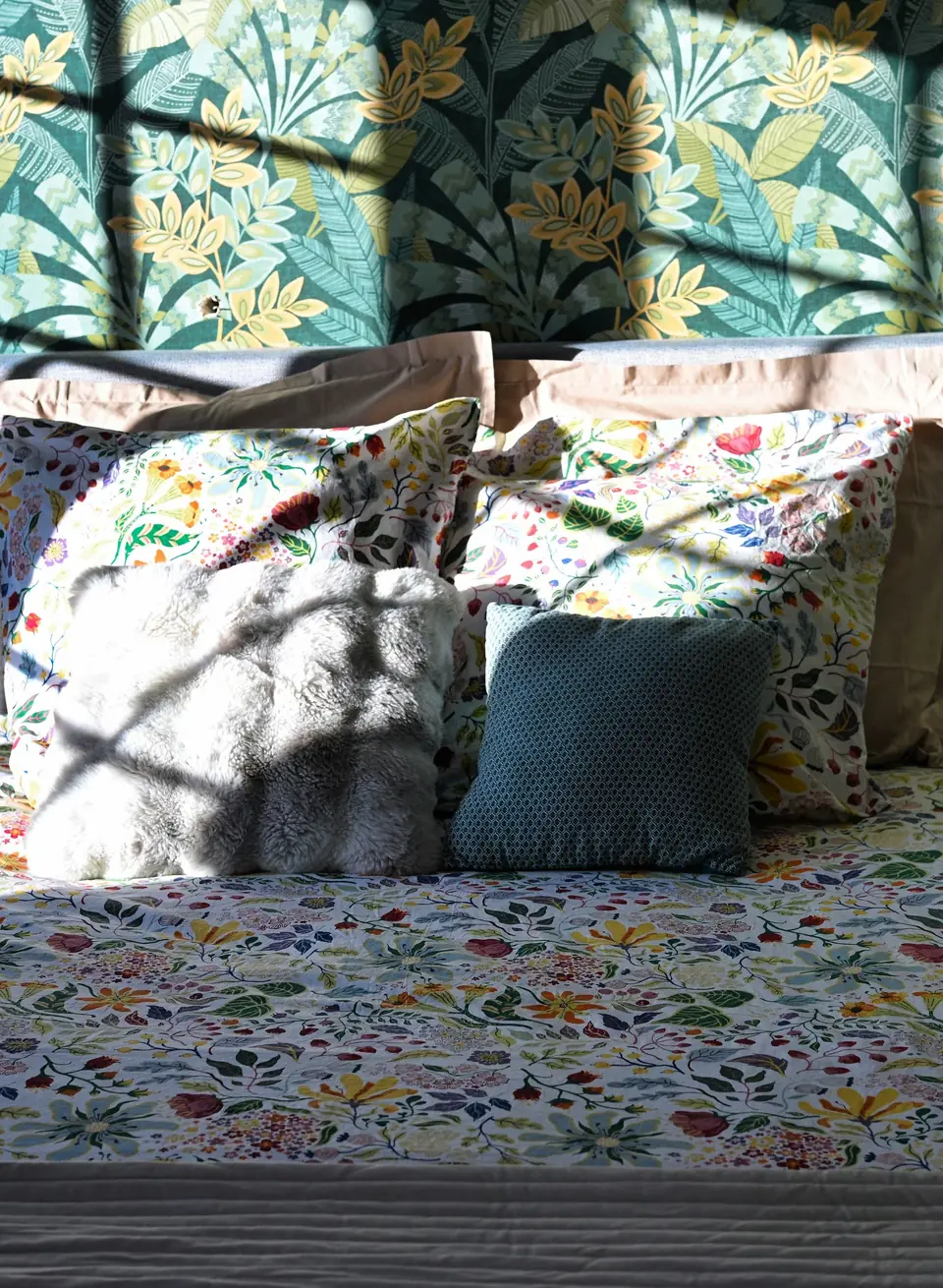 Une chambre du Chalet Normand : le lit au couvre-lit fleuri devant un papier peint de feuillages, dans un rayon de soleil